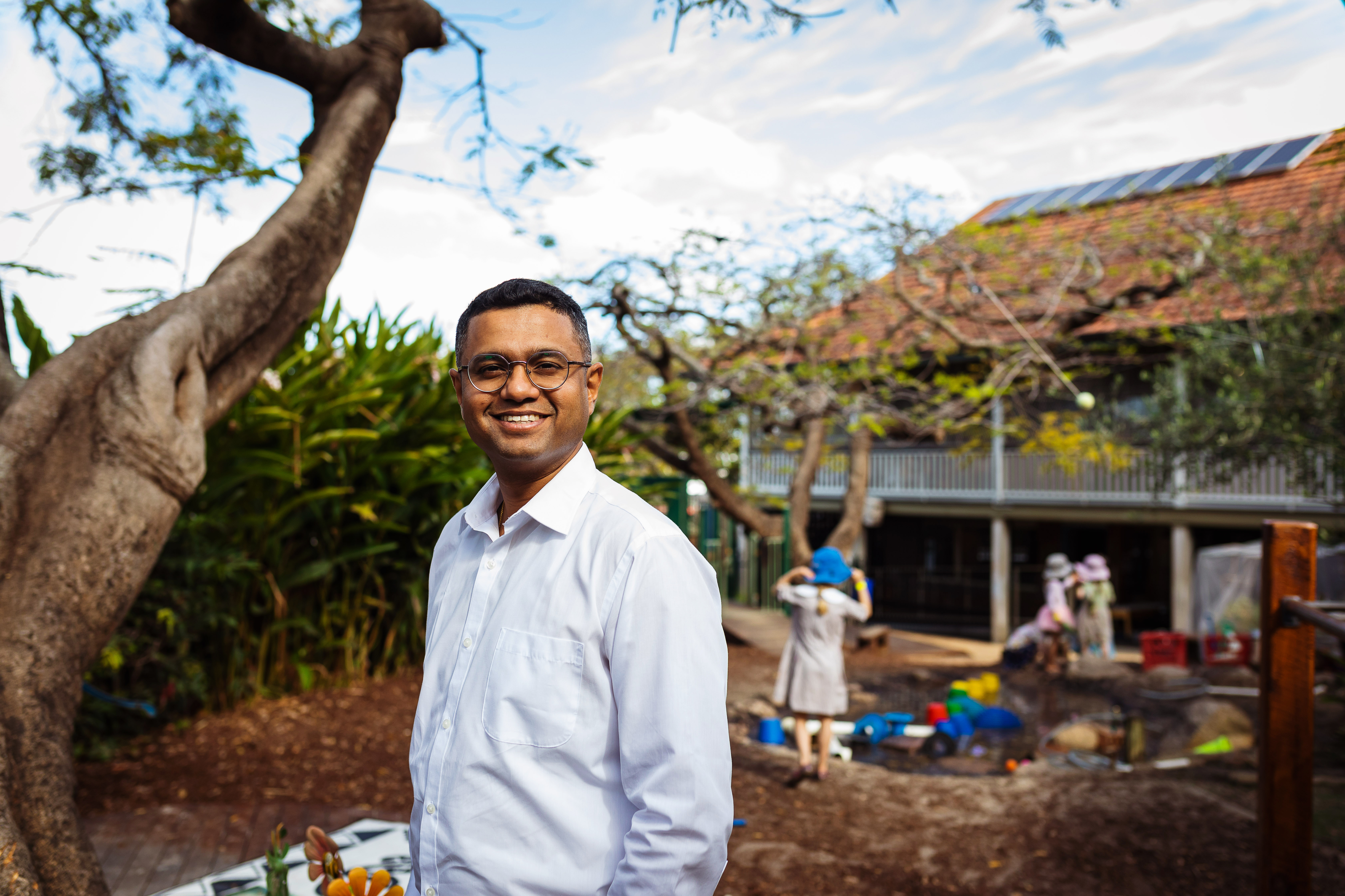 Man in outdoor kindergarten space smiling looking at camera. Playground in the background