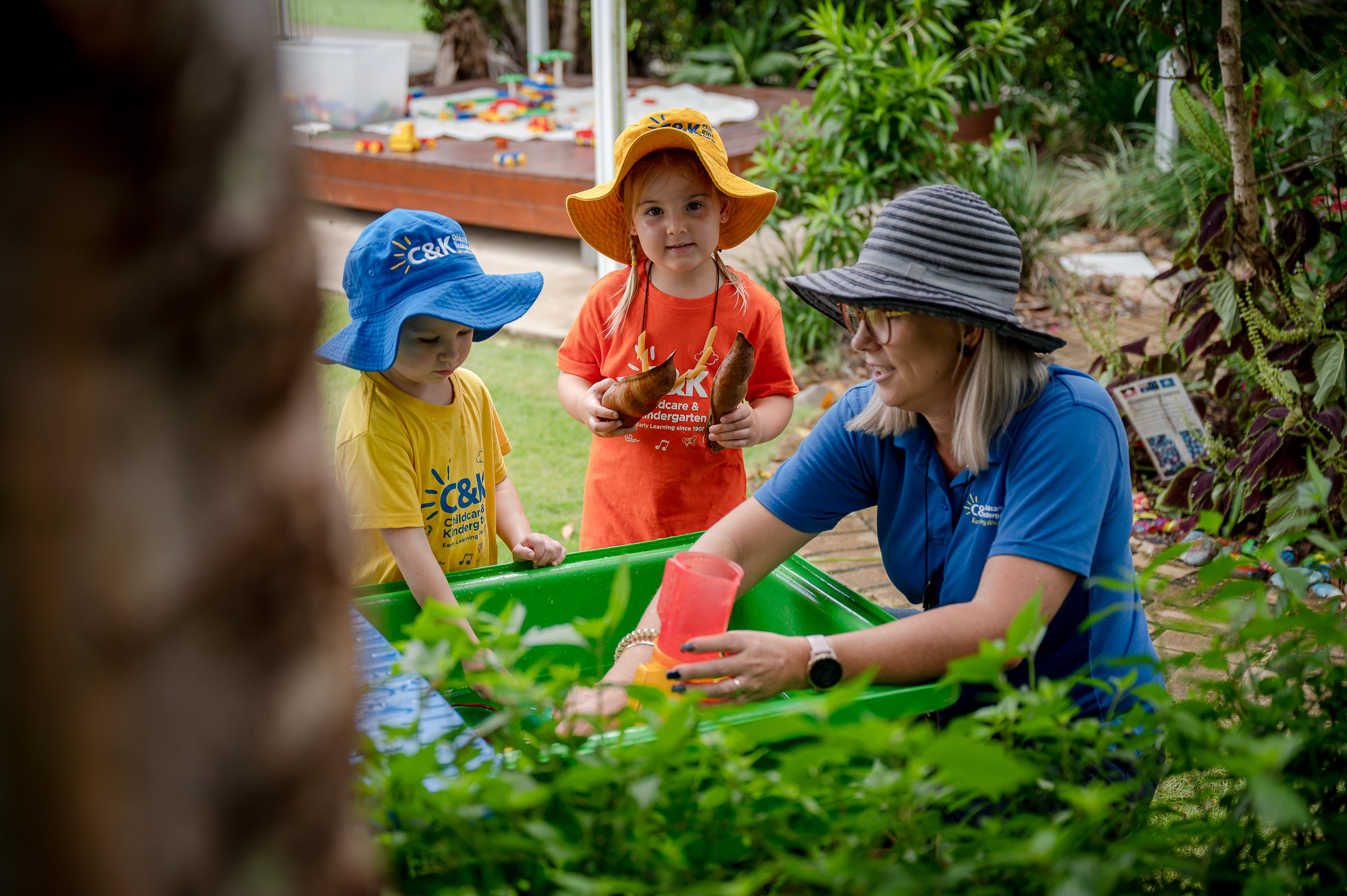 An educator with two children all wearing hats playing in veggie garden